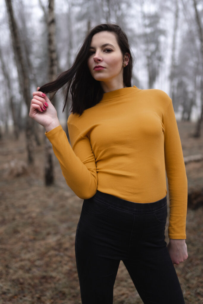 portret fotografie mlada zena holka bruneta divka hnede vlasy stojici oranzove triko v zime zima drzi si vlasy